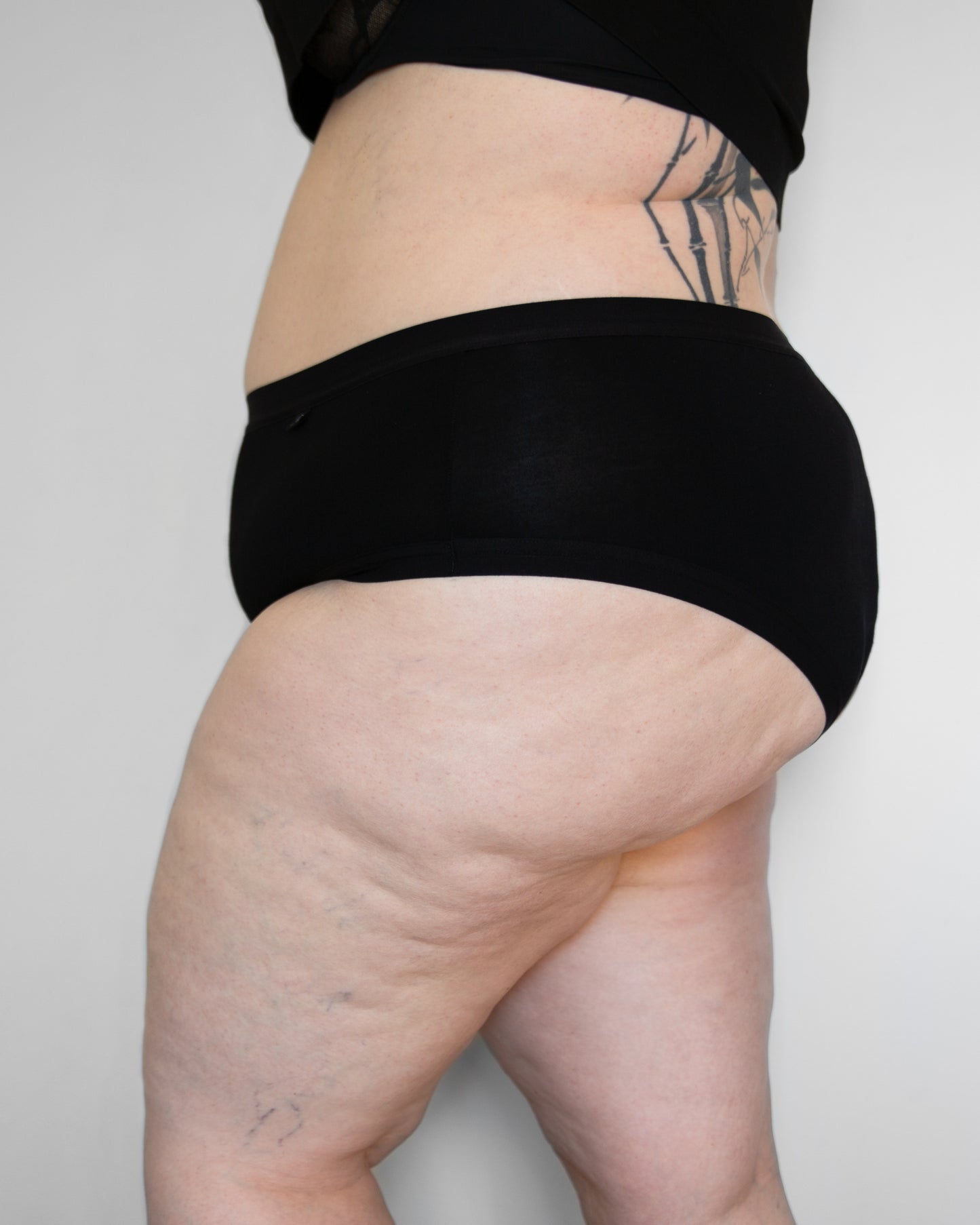 Side view of a model wearing The Bamboo Brazilian in black colour with plain elastic in the leg opening.