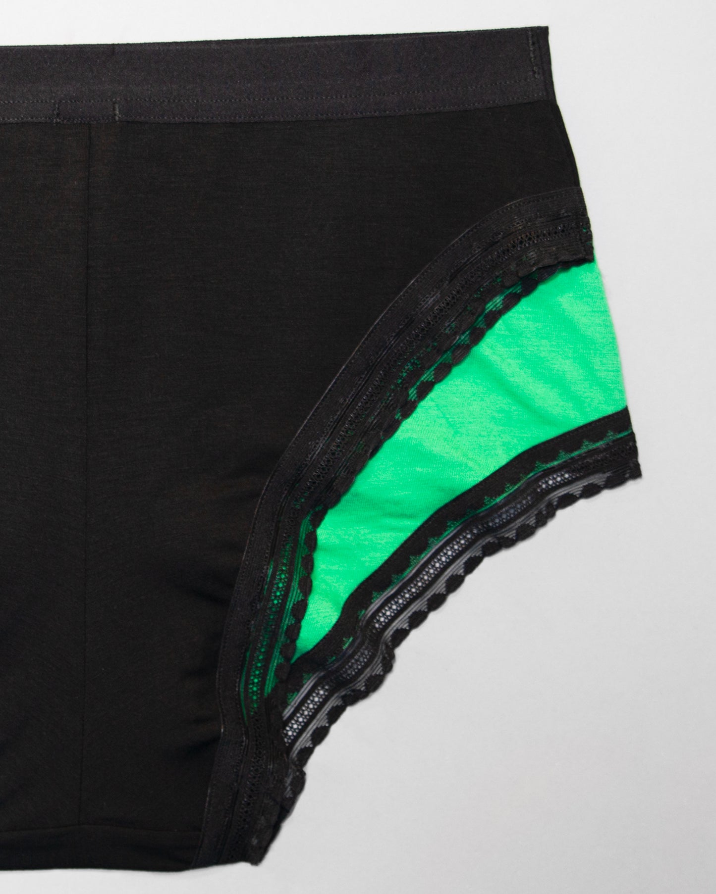 Back view of a sample of The Bamboo High Cut on top of a sample of The Bamboo Hipster, to compare the leg opening shape. The Bamboo High Cut has a smaller side seam, making the leg opening less covering.