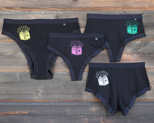 Four pairs of underweart on a rustic wooden background, each featuring a different colored book graphic; yellow, magenta, green and white. This is The Book print!