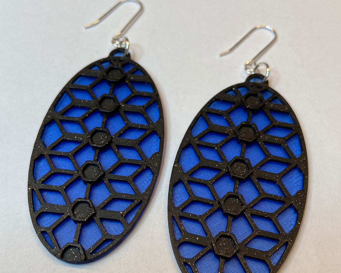 A closeup photo of a pair of 3D-printed earrings with a lace inspiered design. The black colour has glittering flakes.