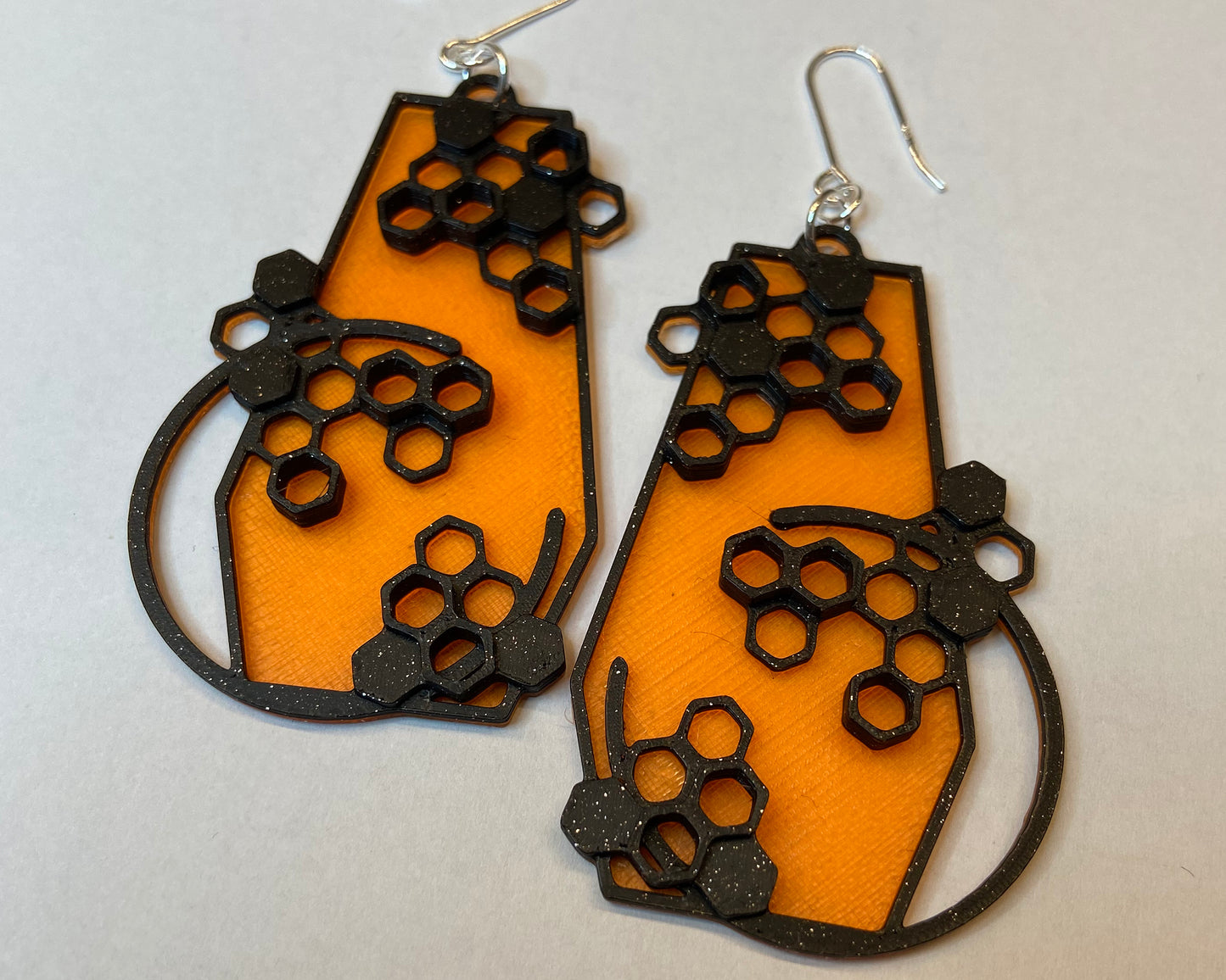 A closeup photo of a pair of 3D-printed earrings with a honeycomb design. The black colour has glittering flakes.