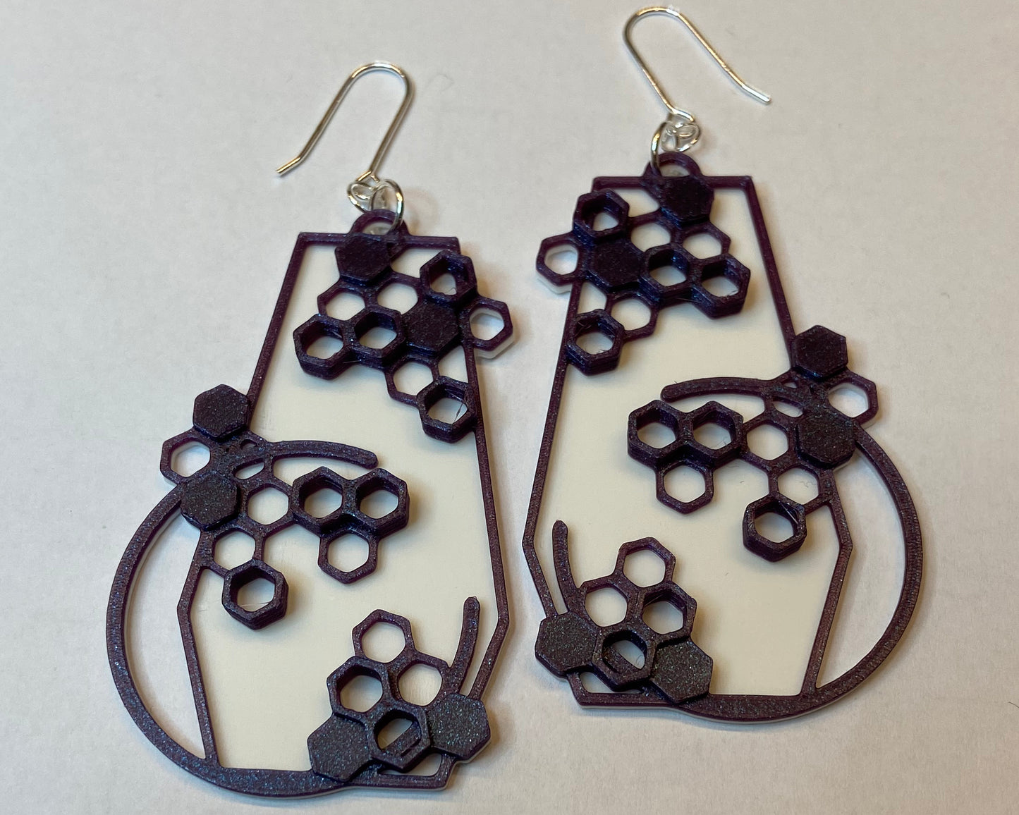 A closeup photo of a pair of 3D-printed earrings with a honeycomb design. The purple colour has a beautiful shimmering effect.