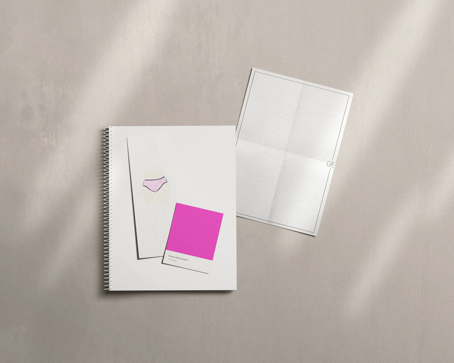 An example of how to use a fashion croquis. Ontop of a spiral notbook is a drawn figuer is wearing a pink knicker and next to the skecth is a colour card for a pink colur. Next to the notebook is a page from the Free download.
