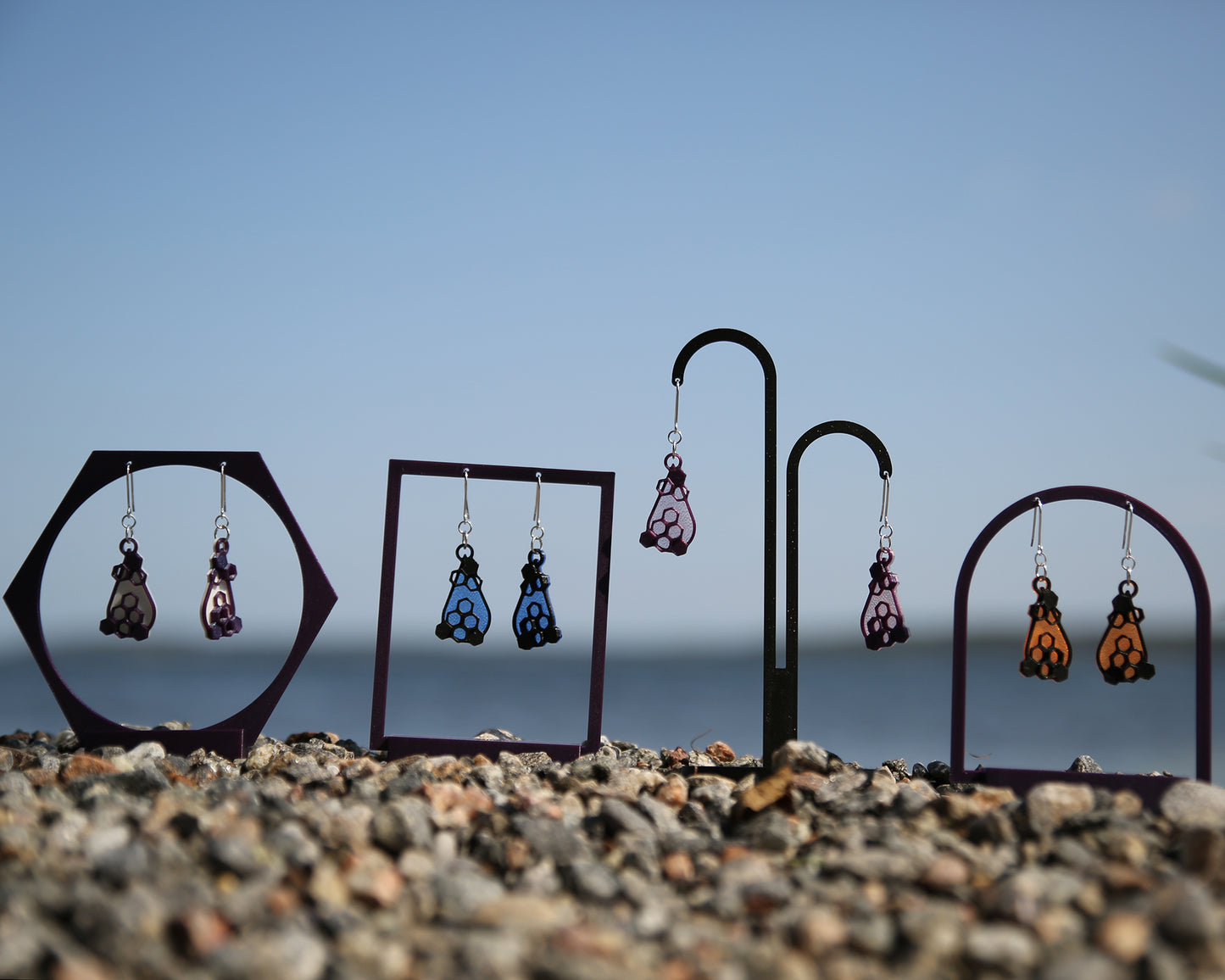 Colorful earrings with a honeycomb design, displayed on stands against a blue sky and rocky ground.