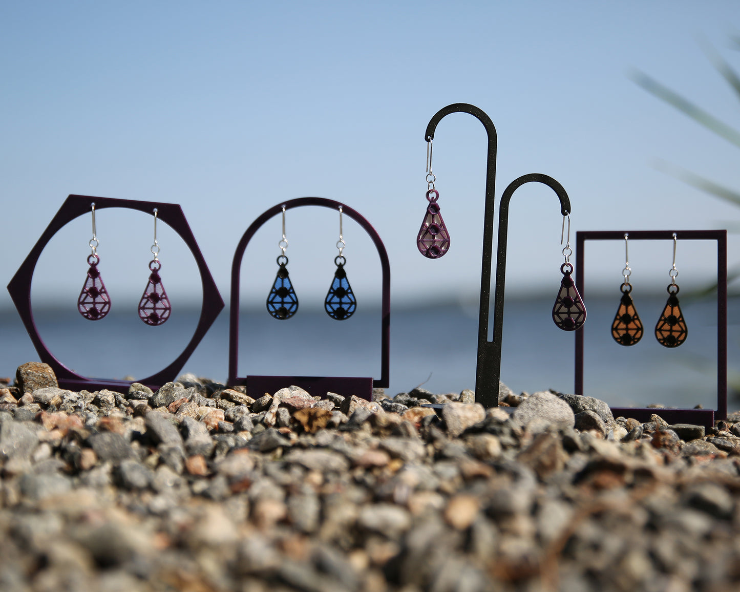 Colorful earrings with a lace inspiered design, displayed on stands against a blue sky and rocky ground.