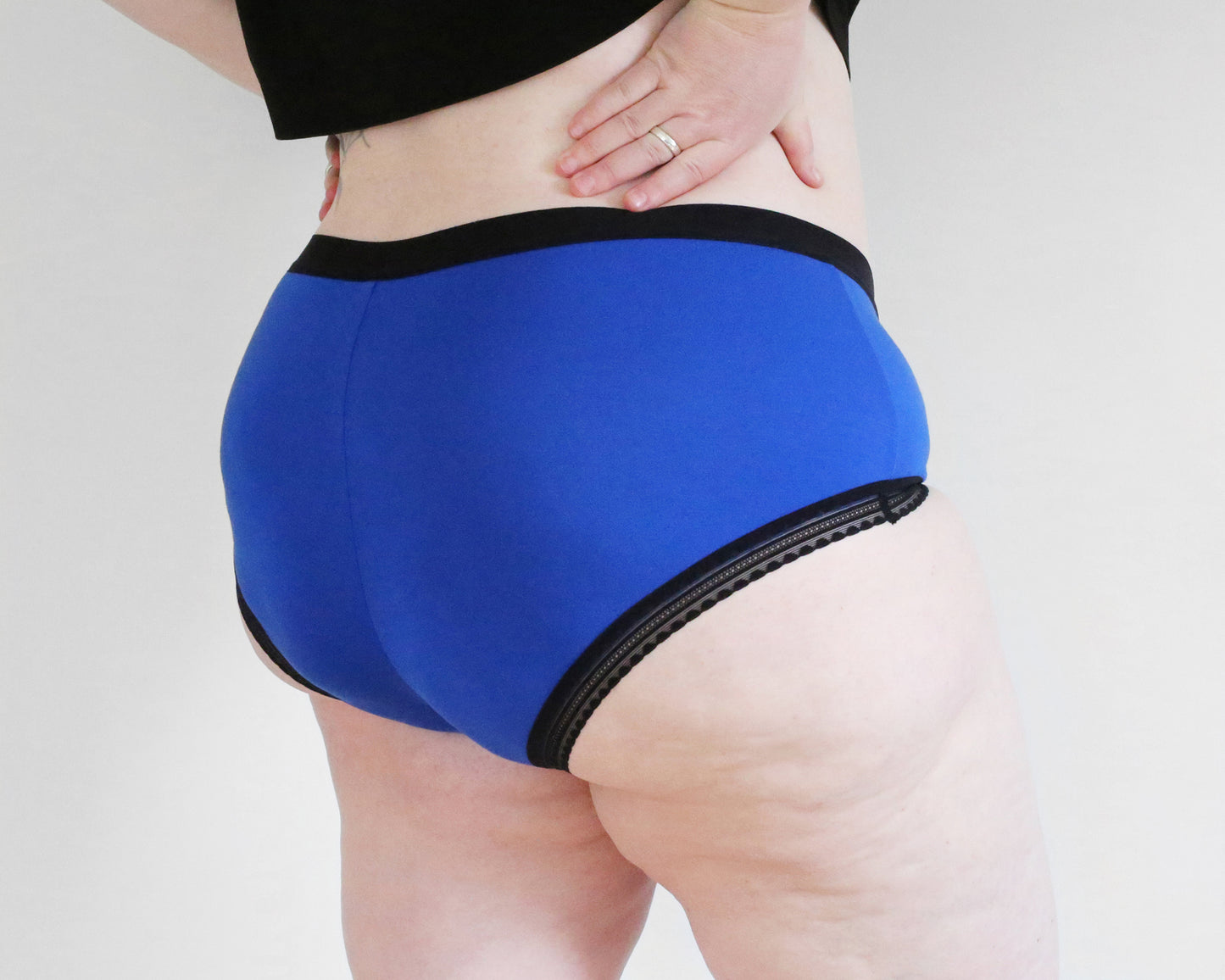 Back side view of a model wearing The Bamboo Hipster - Limited Edition in blue colour and black trims, hands on her lower back.