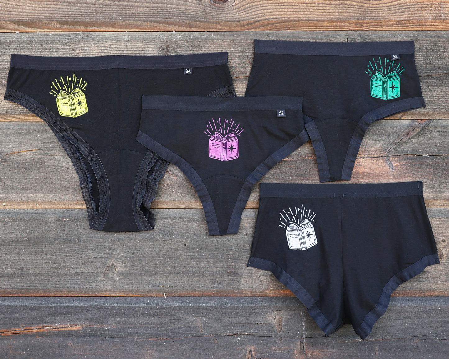 Four pairs of underweart on a rustic wooden background, each featuring a different colored book graphic; yellow, magenta, green and white. This is The Book print!