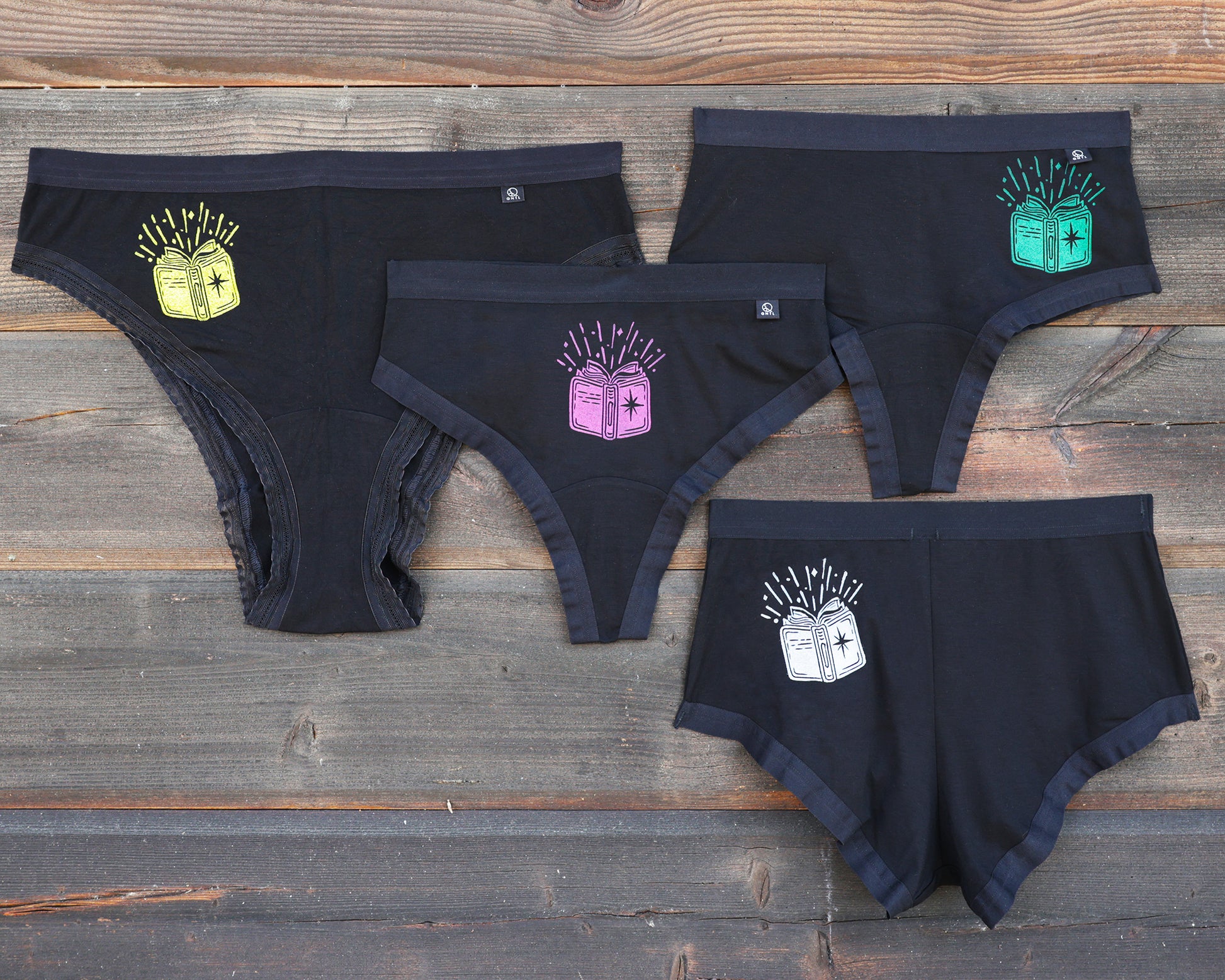 Four pairs of underweart on a rustic wooden background, each featuring a different colored book graphic; yellow, magenta, green and white. This is The Book print!