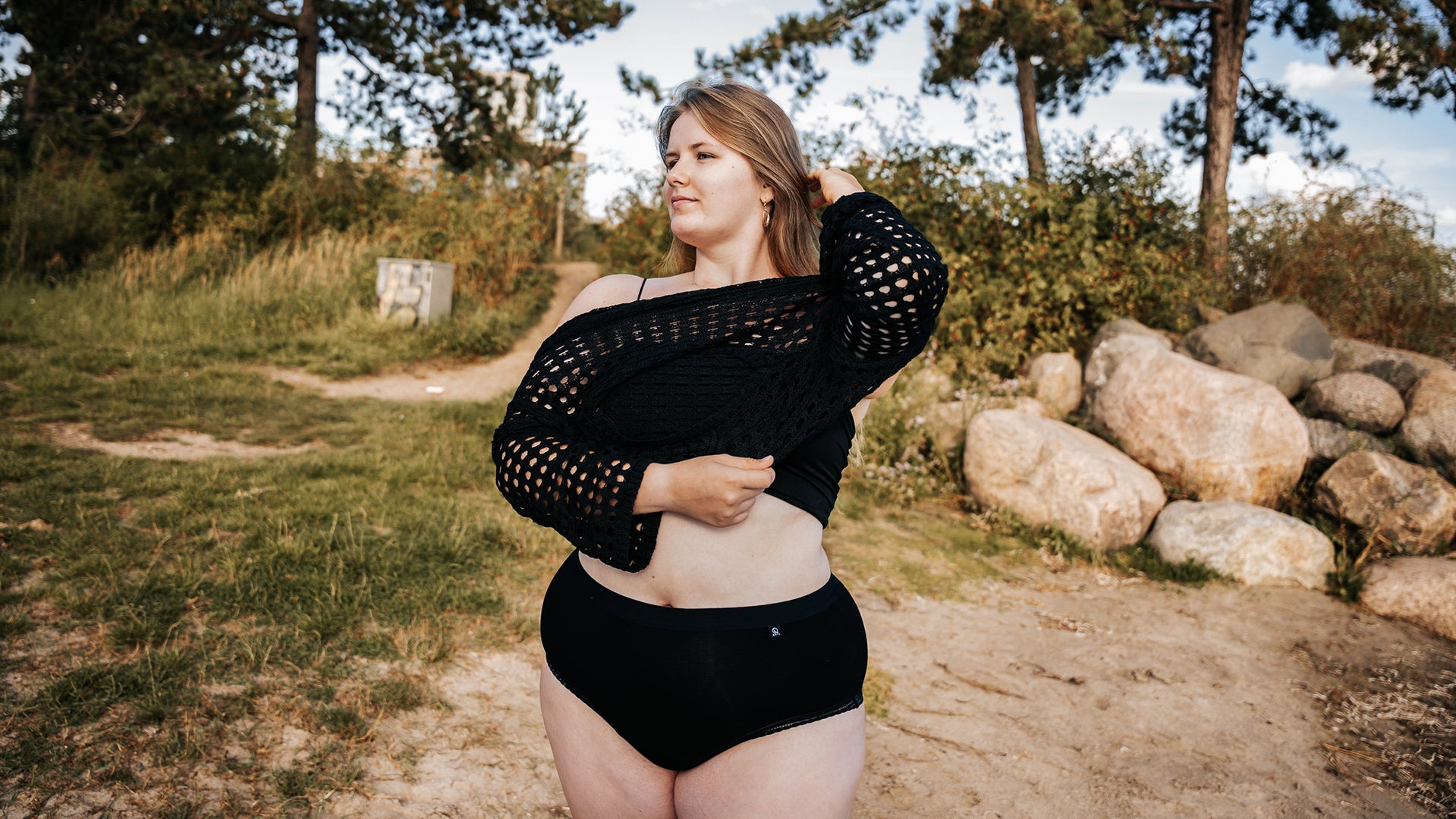 Model wearing The Bamboo Hipster, putting on a sweater on the beach facing viewer.