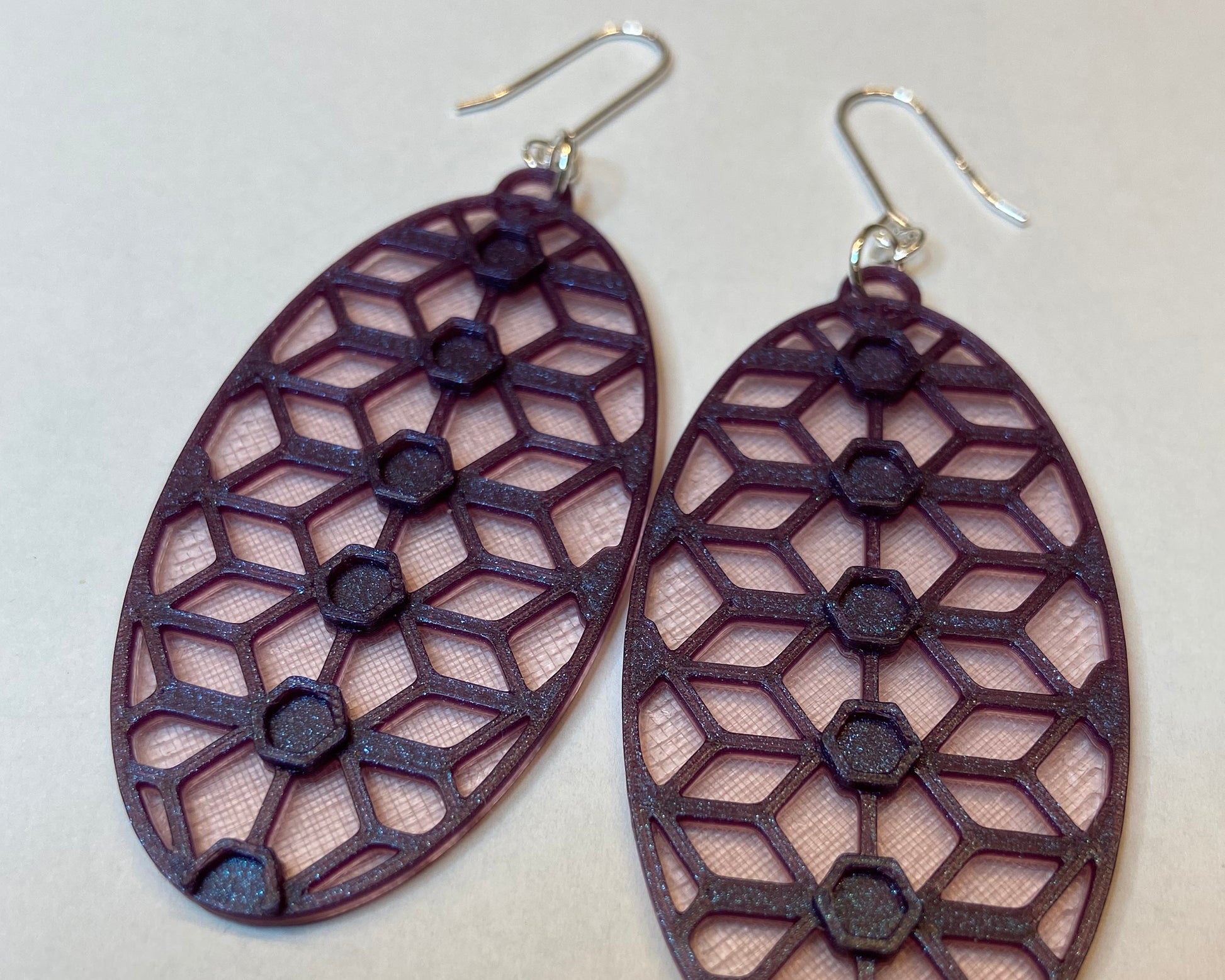 A closeup photo of a pair of 3D-printed earrings with a lace inspiered design. The purple colour has a beautiful shimmering effect. 