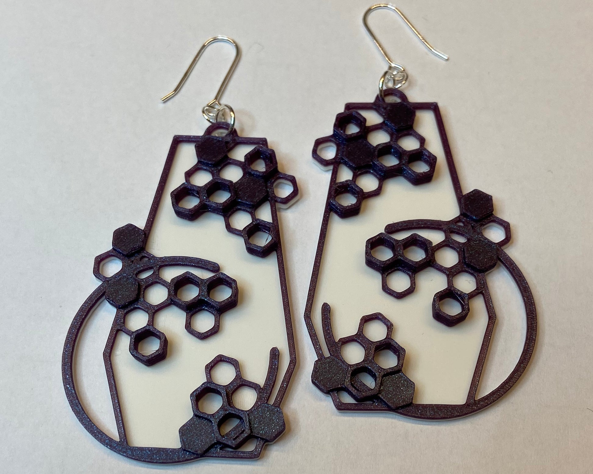 A closeup photo of a pair of 3D-printed earrings with a honeycomb design. The purple colour has a beautiful shimmering effect. 