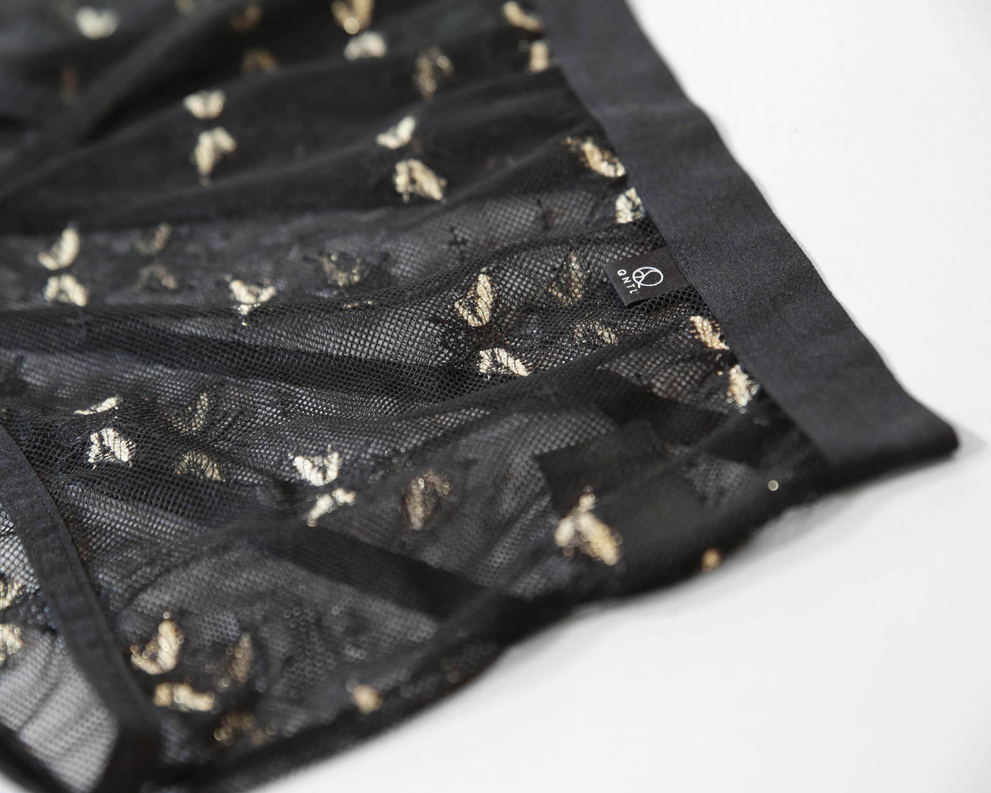 Closeup of the gold pattern colour option, showing the bees with golden wings in the lace and brand label with the QNTL logo.