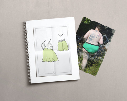Drawing of a babydoll dress on a croquies, ontop of a notebook and a photo of a model wearing green knickers.